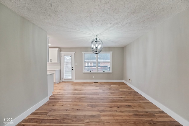 unfurnished dining area with a notable chandelier, light wood-type flooring, and a textured ceiling