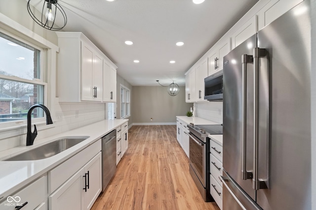 kitchen featuring decorative light fixtures, white cabinetry, sink, and appliances with stainless steel finishes