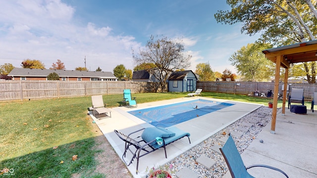 view of pool featuring a lawn, a patio area, and a storage shed