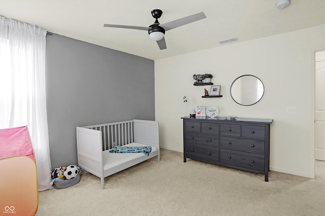 carpeted bedroom featuring a nursery area and ceiling fan