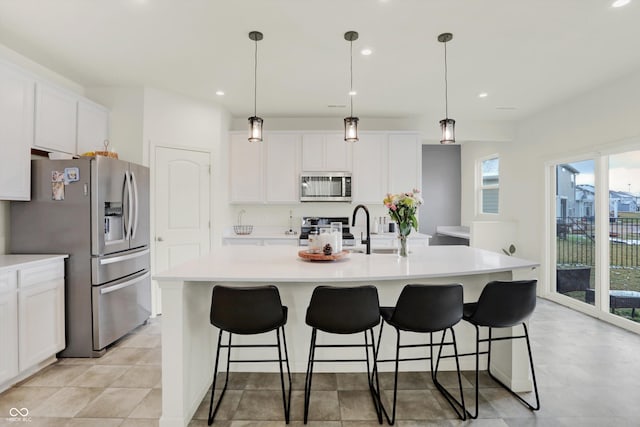 kitchen featuring a center island with sink, pendant lighting, white cabinetry, and appliances with stainless steel finishes