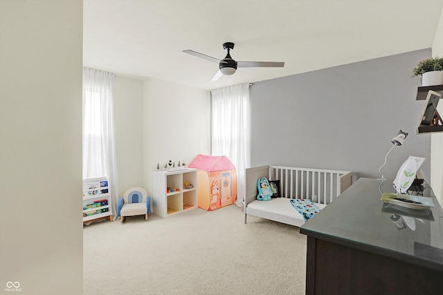 bedroom featuring multiple windows, ceiling fan, carpet floors, and a nursery area