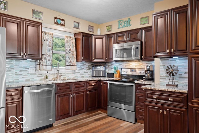 kitchen with sink, light wood-type flooring, appliances with stainless steel finishes, tasteful backsplash, and light stone counters