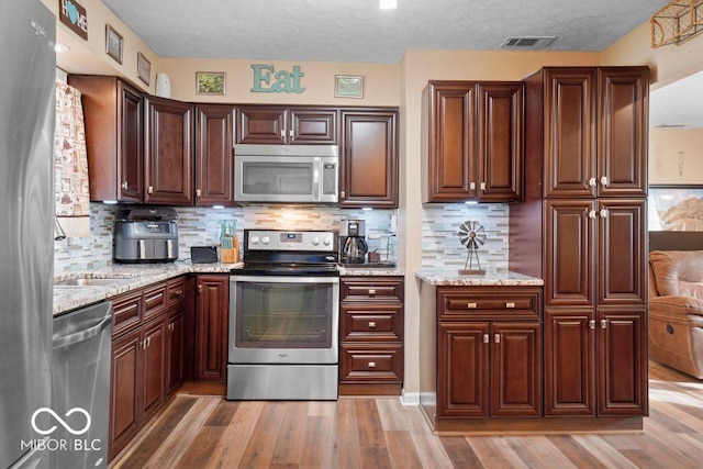 kitchen featuring light stone countertops, tasteful backsplash, light hardwood / wood-style flooring, a textured ceiling, and appliances with stainless steel finishes