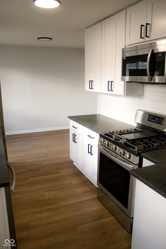 kitchen with stainless steel appliances, white cabinetry, dark wood-type flooring, and dark stone countertops