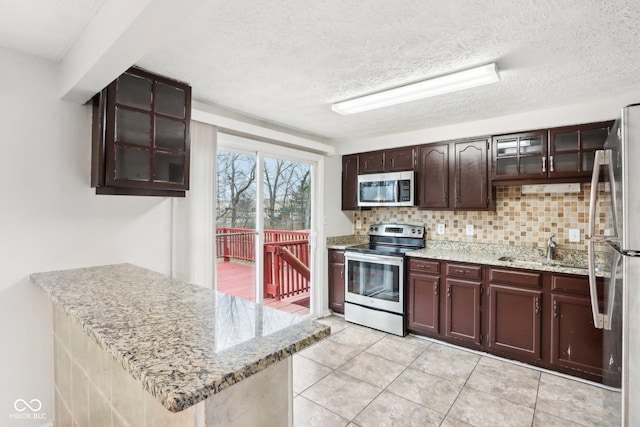 kitchen with stainless steel appliances, light stone countertops, a textured ceiling, and backsplash