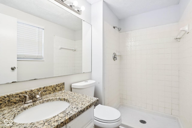 bathroom featuring vanity, toilet, tiled shower, and a textured ceiling