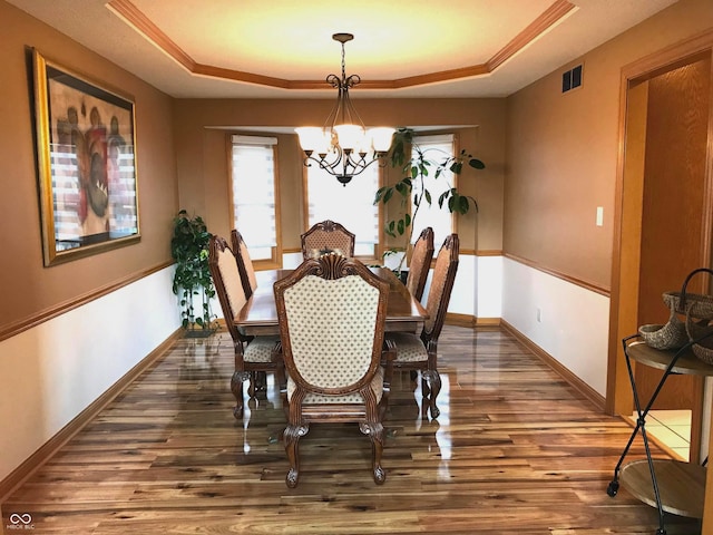 dining space with a chandelier, a tray ceiling, and dark wood-type flooring