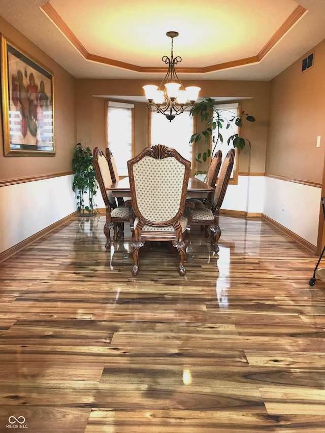 dining area with hardwood / wood-style floors, a raised ceiling, and a chandelier