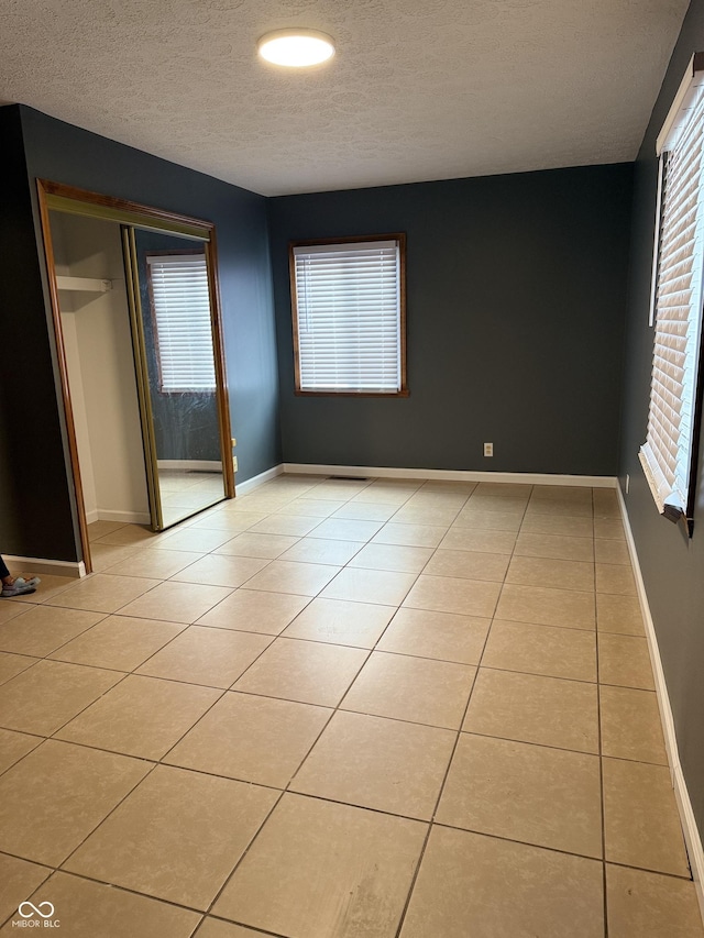 spare room with light tile patterned flooring, a healthy amount of sunlight, and a textured ceiling