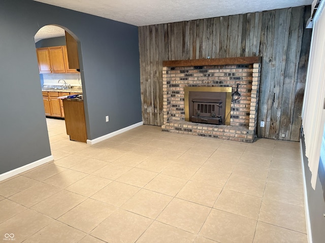 unfurnished living room with a fireplace, light tile patterned floors, a textured ceiling, and wood walls