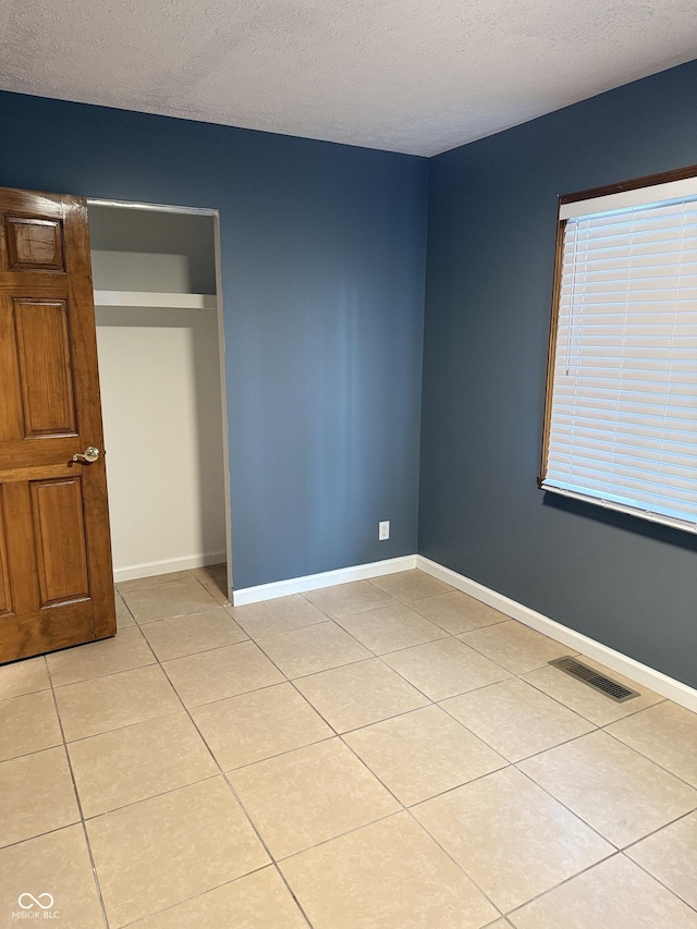 unfurnished bedroom featuring light tile patterned flooring, a textured ceiling, and a closet