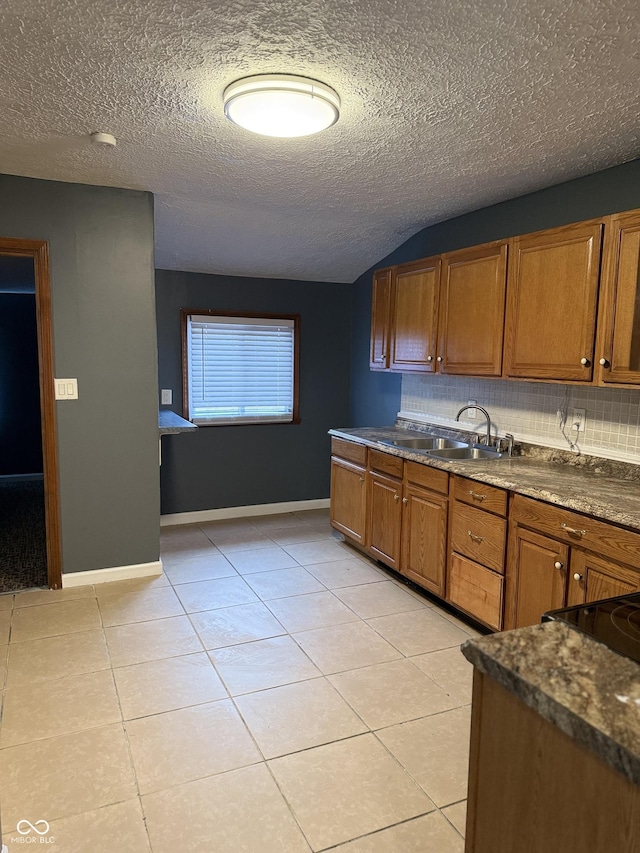 kitchen with a textured ceiling, light tile patterned flooring, sink, and dark stone counters