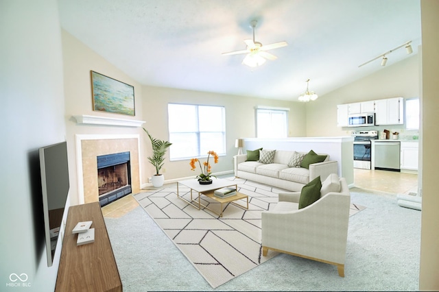 living room featuring ceiling fan with notable chandelier, rail lighting, vaulted ceiling, light tile patterned floors, and a tiled fireplace