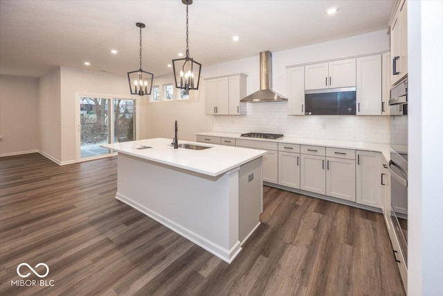 kitchen with pendant lighting, sink, wall chimney range hood, and an island with sink