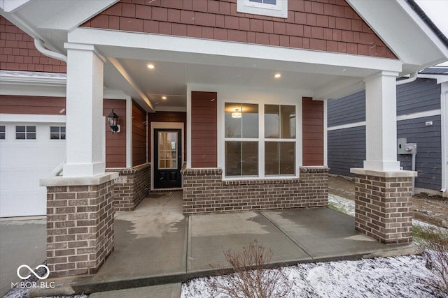 snow covered property entrance featuring covered porch and a garage