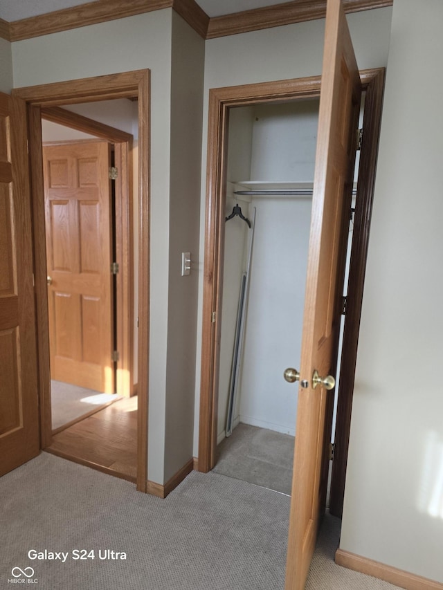 corridor featuring light carpet, baseboards, and ornamental molding