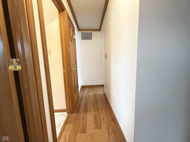 hallway with baseboards, light wood-type flooring, visible vents, and crown molding