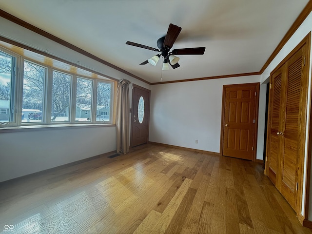 interior space featuring baseboards, ceiling fan, light wood-type flooring, and crown molding