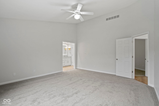 unfurnished bedroom with carpet, ceiling fan, ensuite bathroom, and a high ceiling