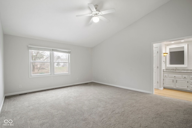 unfurnished bedroom with ensuite bath, ceiling fan, sink, high vaulted ceiling, and light colored carpet