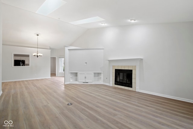 unfurnished living room with vaulted ceiling with skylight, light hardwood / wood-style flooring, a fireplace, and an inviting chandelier