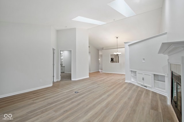 unfurnished living room with a skylight, high vaulted ceiling, light hardwood / wood-style floors, and a notable chandelier