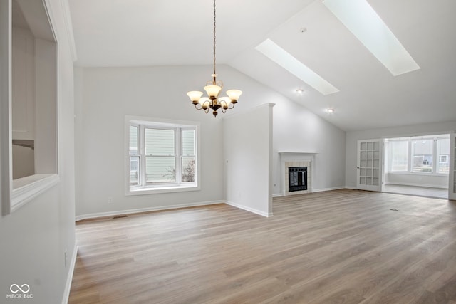 unfurnished living room featuring a skylight, a tile fireplace, high vaulted ceiling, a chandelier, and light hardwood / wood-style floors