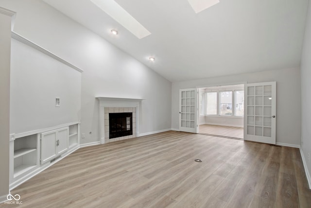 unfurnished living room featuring light wood-type flooring, a tiled fireplace, french doors, and a skylight