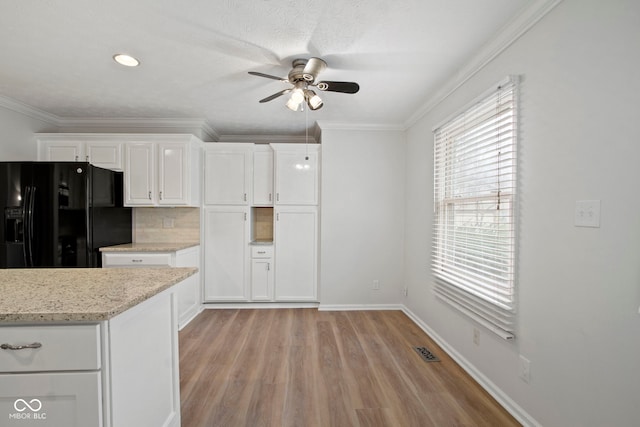 kitchen with white cabinetry, backsplash, black fridge, and crown molding