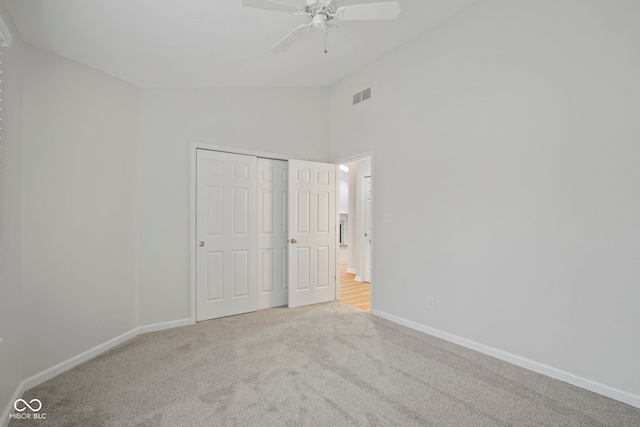 unfurnished bedroom with ceiling fan, light colored carpet, high vaulted ceiling, and a closet