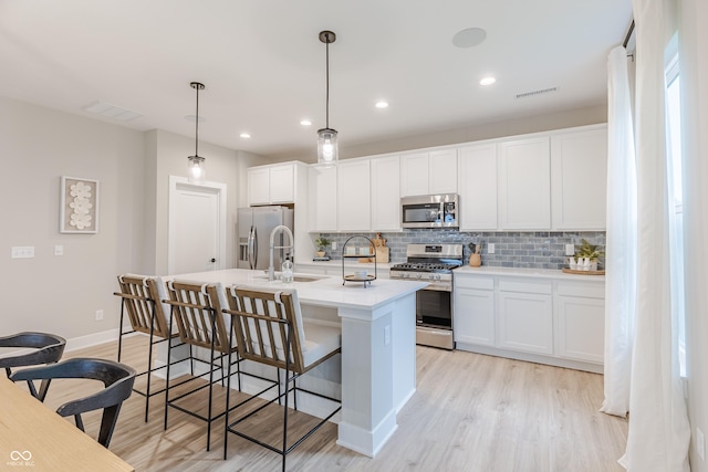 kitchen with white cabinetry, a kitchen island with sink, hanging light fixtures, and stainless steel appliances