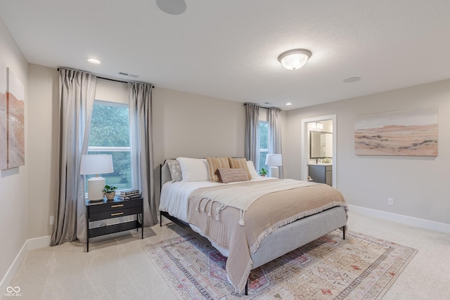 bedroom with ensuite bath, light colored carpet, and multiple windows