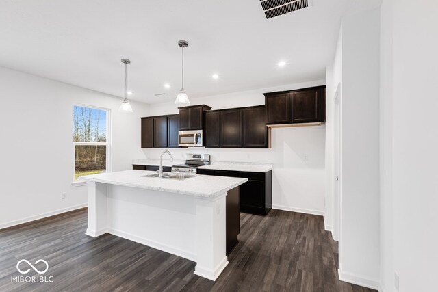 kitchen featuring a sink, visible vents, hanging light fixtures, appliances with stainless steel finishes, and a center island with sink