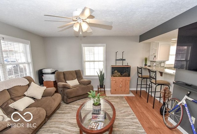 living room featuring a wealth of natural light, ceiling fan, a textured ceiling, and light wood-type flooring