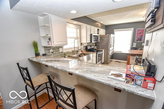 kitchen featuring white cabinets, appliances with stainless steel finishes, light stone countertops, and a breakfast bar area