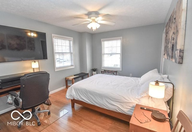 bedroom with multiple windows, wood-type flooring, a textured ceiling, and ceiling fan