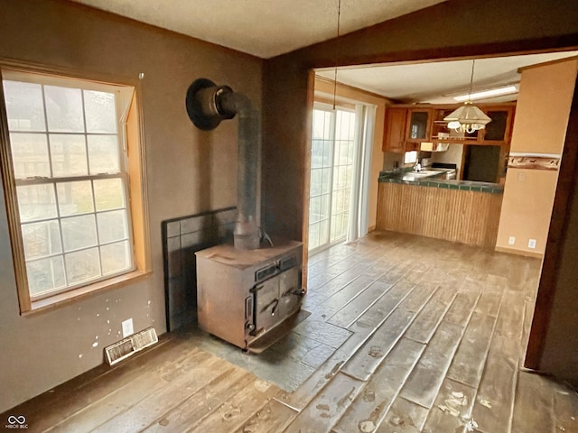 kitchen featuring wood-type flooring, decorative light fixtures, vaulted ceiling, and a wood stove