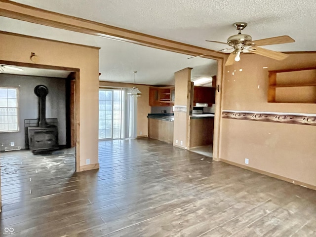 unfurnished living room featuring ceiling fan, dark hardwood / wood-style flooring, plenty of natural light, and a wood stove