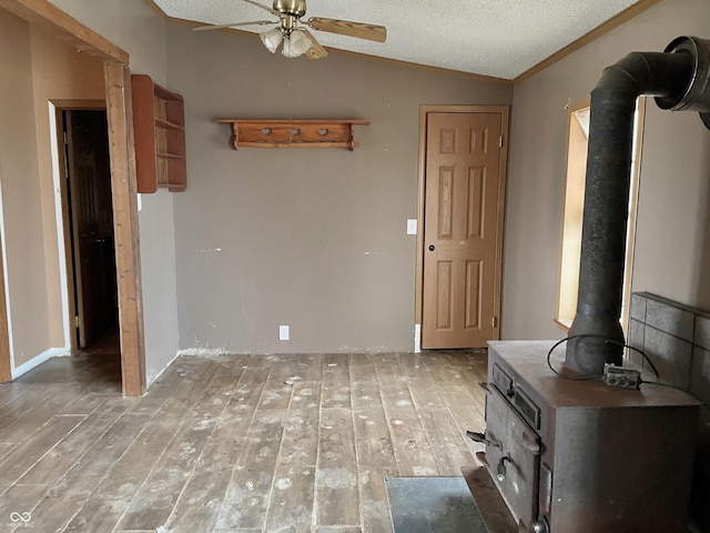 unfurnished living room with vaulted ceiling, hardwood / wood-style flooring, ceiling fan, and a wood stove