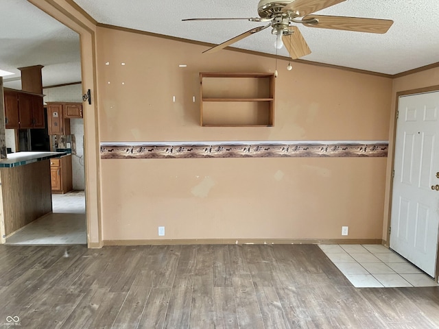 kitchen with a textured ceiling, vaulted ceiling, light hardwood / wood-style flooring, ornamental molding, and ceiling fan