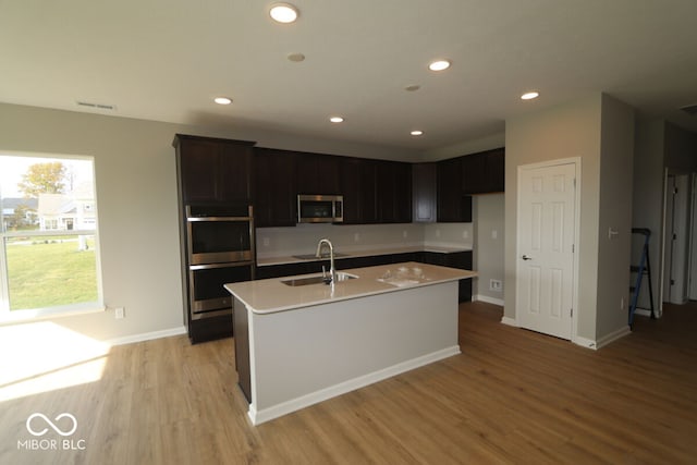 kitchen with appliances with stainless steel finishes, an island with sink, light hardwood / wood-style floors, and sink