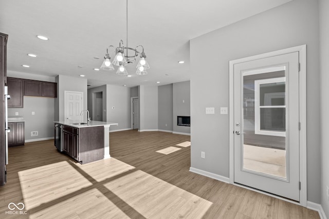 kitchen featuring a center island with sink, sink, light wood-type flooring, pendant lighting, and dark brown cabinetry