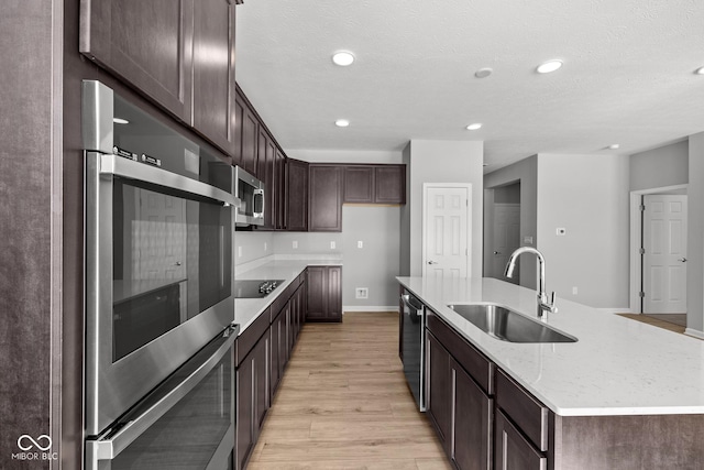 kitchen featuring a center island with sink, sink, light stone counters, light wood-type flooring, and stainless steel appliances