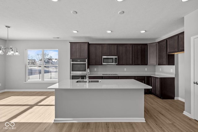 kitchen featuring sink, light wood-type flooring, stainless steel appliances, dark brown cabinetry, and a kitchen island with sink