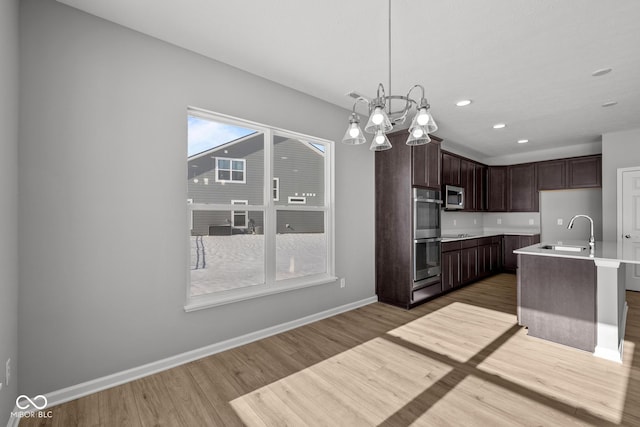 kitchen with dark brown cabinets, light wood-type flooring, decorative light fixtures, sink, and a kitchen island with sink