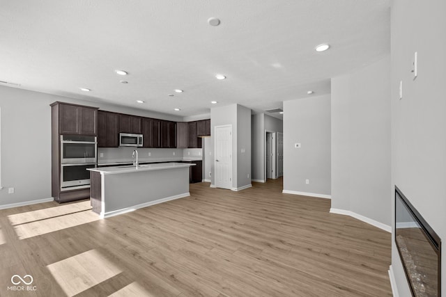 kitchen with appliances with stainless steel finishes, sink, light wood-type flooring, dark brown cabinets, and a kitchen island with sink