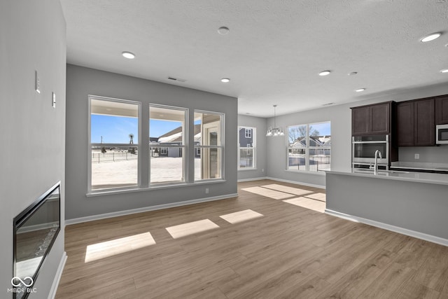 unfurnished living room with sink, a textured ceiling, an inviting chandelier, and light hardwood / wood-style flooring