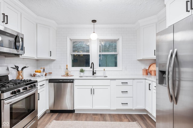 kitchen featuring sink, light hardwood / wood-style floors, pendant lighting, white cabinets, and appliances with stainless steel finishes