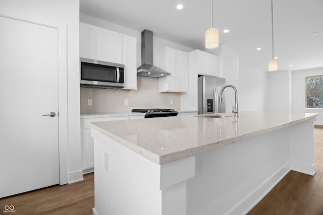 kitchen featuring a kitchen island with sink, pendant lighting, wall chimney exhaust hood, and stainless steel appliances